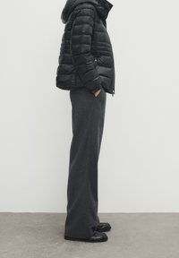 Sort puffjakke med hætte, præget af et kviltet design. Parret med grå bukser med vidde og sorte loafers. Enkel, struktureret silhuet.