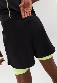 Pantaloni sportivi neri con tasca posteriore con zip, caratterizzati da un tessuto leggero e una fodera interna verde lime che spunta.