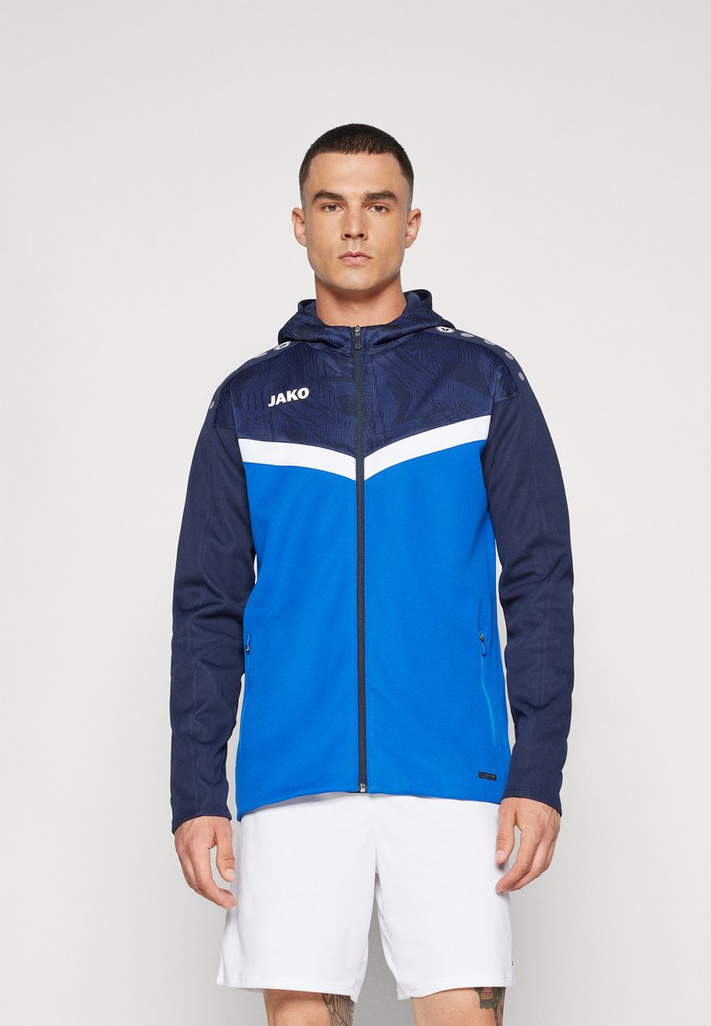 Blue athletic jacket with a hood, featuring a textured navy top panel, white chevron stripe, and side zip pockets.