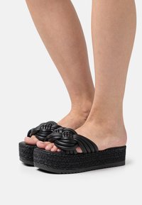 Sandales plateformes noires avec des lanières nouées, dotées d'une semelle tissée texturée et d'une finition lisse. Le design ouvert à l'avant révèle les orteils.