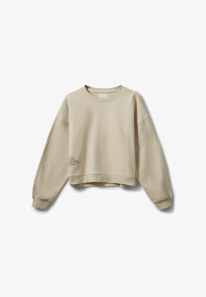 Beež värvitud lühikese lõikega dressipluus pehmest kangast, millel on langenud õlad ja vasakul küljel trükitud tekstiga detail. Sile tekstuur.