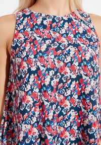 Ärmlös klänning med rund halsringning som har ett tätt blommönster i rött, vitt, blått och rosa mot en mörkblå bakgrund.
