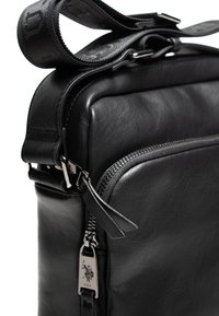 Borsa in pelle nera con una superficie liscia, dotata di chiusura con zip, accessori resistenti e una tracolla regolabile per opzioni di trasporto versatili.