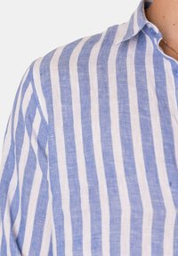 Camicia di lino a righe verticali blu e bianche, con colletto a punta, pattina con bottoni e tessuto testurizzato.