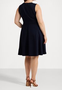 Námořnické bezrukávové šaty s přiléhavým vrškem a rozšířenou sukní, s nenápadným zipem na zadní straně a hladkým textilním povrchem. Hnědé sandály na vysokém podpatku.