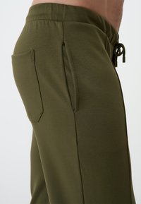 Olive green joggers made from soft fabric, featuring a side pocket, elastic waistband, and adjustable drawstring. Smooth texture and modern fit.