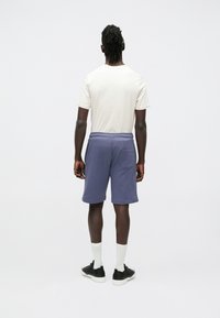 Bomulds-T-shirt i off-white, kombineret med lilla fleece-shorts med elastisk talje og en baglomme. Sorte sneakers og hvide sokker.