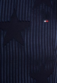 Tissu texturé bleu marine avec des rayures verticales et de grands motifs d'étoiles, orné d'un petit logo rouge, blanc et bleu.