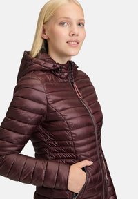 Mørkerød pufferjakke med hætte, lynlås foran og stribet tekstur. Har elastiske manchetter og en snøret talje for et tætsiddende look.