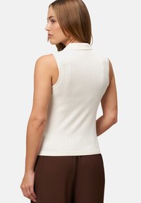 Top bianco a coste senza maniche con colletto, caratterizzato da un design aderente e una consistenza liscia, abbinato a pantaloni marroni.
