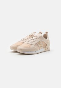 Light beige athletic shoes with mesh and synthetic overlays, round toe, textured sole, gold accents, and laces in matching color.