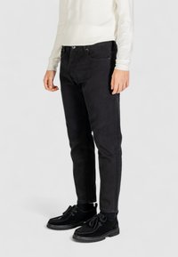 Jeans neri slim-fit in cotone, caratterizzati da un classico design a cinque tasche, cuciture visibili e chiusura a bottone in vita.