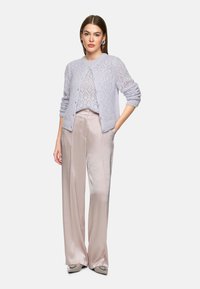 Light lavender knitted cardigan with a diamond pattern, worn over a matching top, paired with smooth, pale pink wide-leg trousers.