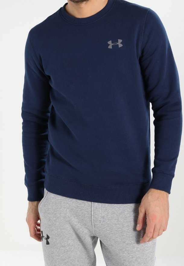 Homme portant un sweat-shirt à manches longues bleu marine et un pantalon de survêtement gris clair, tous deux avec des logos Under Armour visibles.