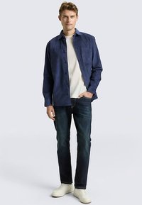 Marineblauw overhemd met knopen en een zak, wit T-shirt met ronde hals, donkerblauwe spijkerbroek en witte sneakers. Soepele stof met een casual pasvorm.