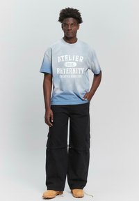 Blue gradient t-shirt with white text, features a round neck, short sleeves. Paired with black cargo pants and tan work boots.