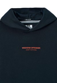 Námornícky sveter s oranžovým textom "WEEKEND OFFENDER ADMIT NOTHING" na hrudi a s etiketou vo vnútri goliera s tým istým nápisom.