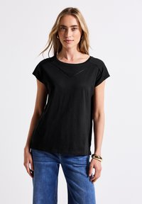 T-shirt noir à manches courtes avec un col rond, présentant un design cousu subtil au niveau de la poitrine. Tissu doux avec une coupe décontractée.
