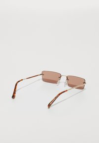 Lunettes de soleil rectangulaires avec des verres marron. Monture en métal doré fine, branches avec motif écaille de tortue et plaquettes de nez transparentes. Design léger.