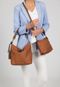 Sac à épaule en similicuir marron avec un design décontracté, une sangle réglable marron, un détail de frange et des accessoires en métal argenté.