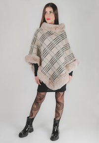 Poncho a scacchi con colori beige, nero e crema. Presenta un morbido colletto e orlo in pelliccia sintetica. Indossato sopra un vestito nero e collant a rete.