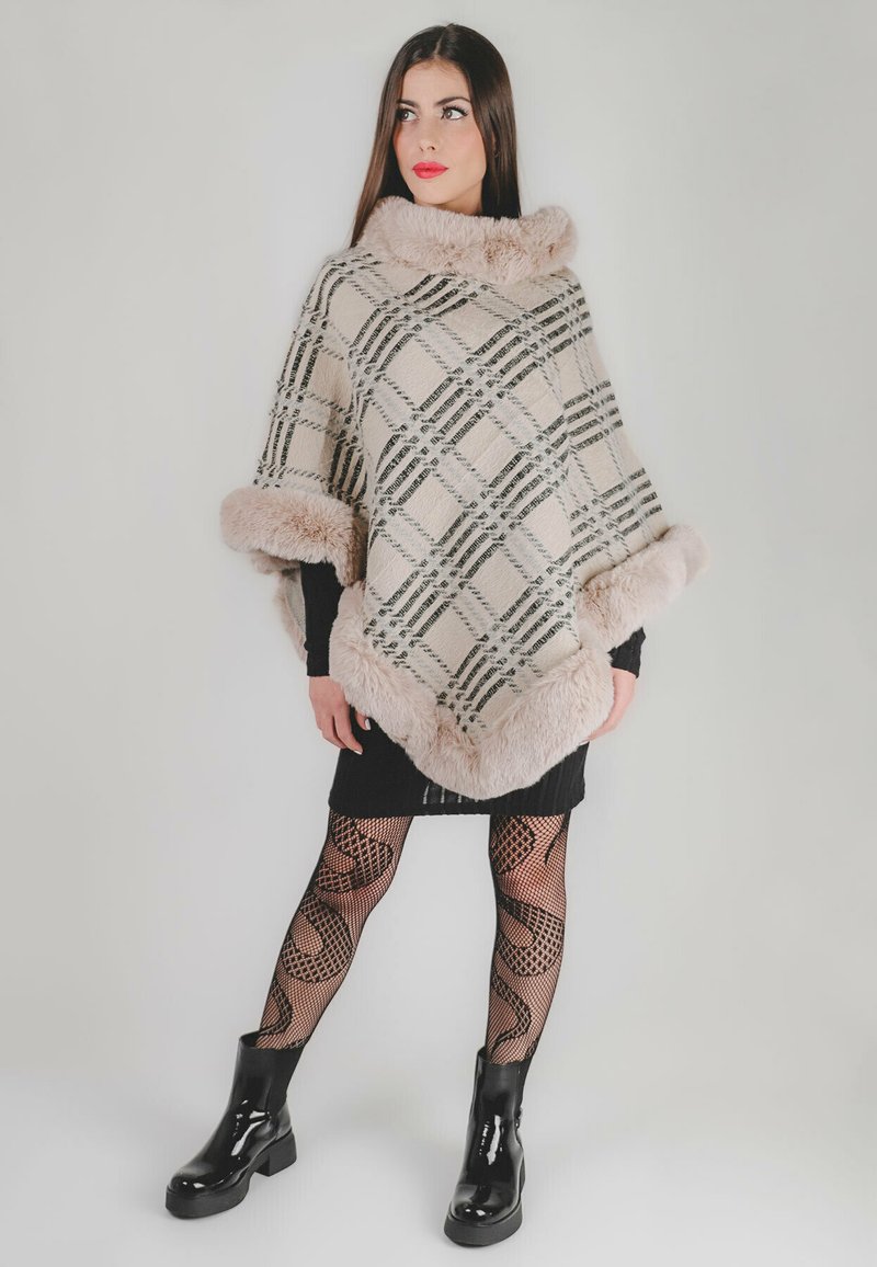 Poncho a scacchi con colori beige, nero e crema. Presenta un morbido colletto e orlo in pelliccia sintetica. Indossato sopra un vestito nero e collant a rete.