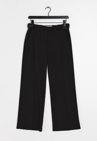 Svarta vida byxor med veck, platt midjeband och sidfickor, hängande på en svart galge mot en vit bakgrund.