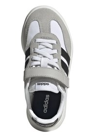 Scarpa sportiva grigia e bianca con tomaia in suede e materiale sintetico, caratterizzata da strisce nere, lacci e una fascia in velcro, con logo sulla linguetta.