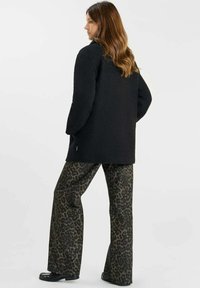 Zwarte fleece jack met een ontspannen pasvorm, lange mouwen en zijzakken. Gecombineerd met bruin panterprint flare-broeken en zwarte schoenen.