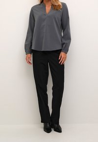 Haut gris à manches longues avec un col en V, associé à un pantalon noir à jambes droites et des chaussures noires pointues. Tissu lisse avec une légère brillance.