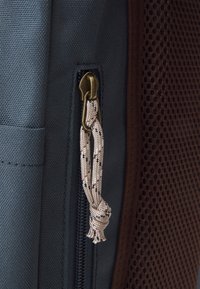 Bolso azul marino con una tela texturizada y un lado de malla marrón. Cuenta con un cierre de bronce con un tirador de tela estampada.