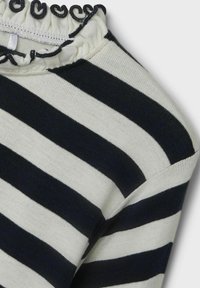 Sweter w paski w kolorach granatowym i kremowym, z prążkowanym kołnierzem z falbaną, o średniej grubości splotu oraz ukośnym szwie na ramieniu.