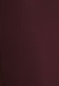 Ribbade burgunderfärgad tyg, medel tjocklek, med vertikala linjer, som erbjuder en texturerad yta. Lämplig för åtsittande plaggdesigns.