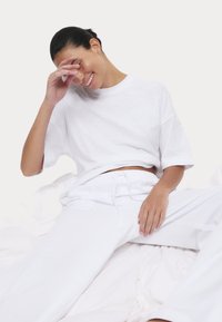 Weißes übergroßes T-Shirt mit rundem Halsausschnitt und kurzen Ärmeln, kombiniert mit passenden weißen Sweatpants, die einen elastischen Bund und Taschen haben.