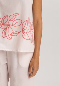 Top de lino blanco con bordado floral en coral a lo largo del dobladillo. La tela es ligera y tiene una textura suave, complementando unos pantalones pastel.