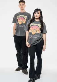 Gray graphic t-shirts featuring a retro Rolling Stones design, worn with black flared pants. The shirts have short sleeves and relaxed fit.