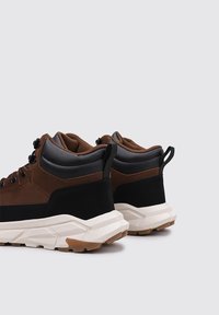 Zapatillas altas marrones y negras con una parte superior de cuero texturizado, cuello acolchado y una gruesa suela de goma blanca con un diseño de desgaste color goma.