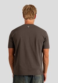 Szara bawełniana koszulka z krótkim rękawem, okrągłym dekoltem i okrągłą metką z logo z tyłu na szyi. Materiał wydaje się gładki i ma luźny fason.