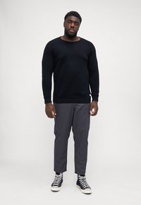Pulover lung negru cu mâneci lungi, cu guler rotund, asortat cu pantaloni cargo gri și adidași negri cu guler înalt, având șireturi albe.