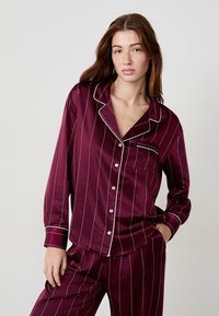 Bordowe piżamy w paski o gładkim satynowym wykończeniu; zawierają koszulę zapinaną na guziki z kieszonką oraz pasujące spodnie z elastycznym pasem.