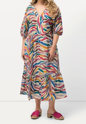 Femme portant une longue robe rayée abstraite multicolore avec des manches ballon jusqu'au coude et des sandales roses à talons ouverts.