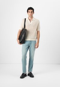 Polo de manga corta de punto en color crema con agujeros decorativos; jeans de color azul claro; bolso tote de cuero negro; zapatos negros.