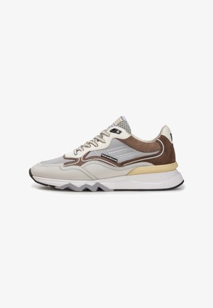 Zapatilla deportiva en beige y marrón que cuenta con materiales de malla y ante, diseño de suela en zigzag y un sistema de cordones destacado con detalle de marca.
