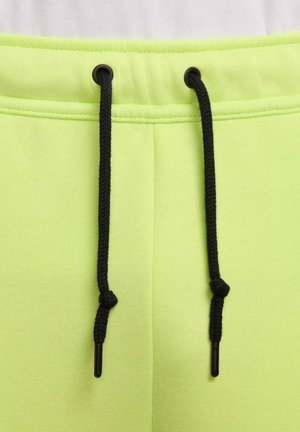 Gomma da jogging verde lime con lacci neri e fermacorda. Tessuto morbido e liscio con cuciture a zig zag, che enfatizzano comfort e vestibilità.
