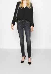 Mustapaita, jossa on nappidetail, yhdistettynä tummiin farkkuihin, joissa on kimaltava paneeli. Mustat korkokengät viimeistelevät asun.