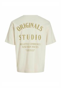 Crème-kleurige katoenen T-shirt met korte mouwen. Bevat grote gouden tekst op de achterkant met de tekst "ORIGINALS STUDIO" en extra kleinere tekst eronder.