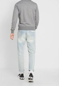 Šedá mikina s dlouhými rukávy, světle modré džíny s vybledlým vzhledem a černé tenisky s bílými akcenty. Ležérní outfit ze zadu.