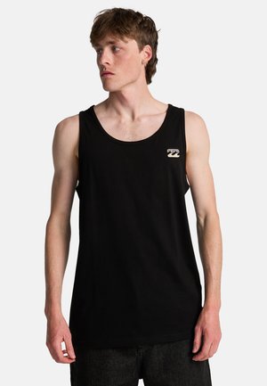 Jeune homme à la peau claire et aux cheveux bruns courts, portant un débardeur noir sans manches avec un petit logo de vague sur la poitrine.