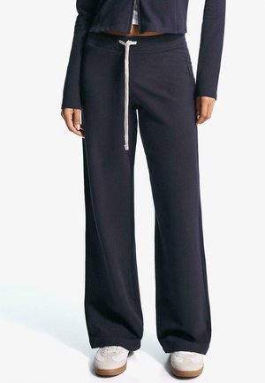 Marineblaue Sweatpants mit weitem Bein, ausgestattet mit einem hellbeigen Kordelzugbund. Hergestellt aus weichem Stoff mit glatter Textur.