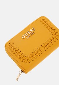 Yellow leather wallet with embossed stitching detail along the edges, featuring a silver logo and a zip closure with a branded zipper pull.